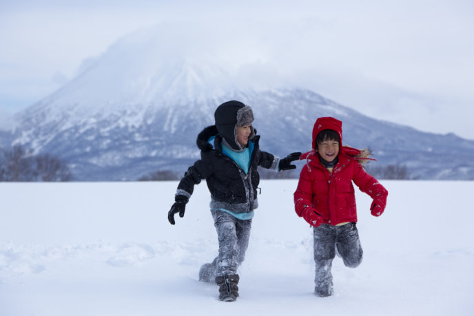 Two Kids Walking On Snow With Mt Yotei In The Background