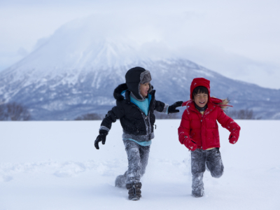 Two Kids Walking On Snow With Mt Yotei In The Background